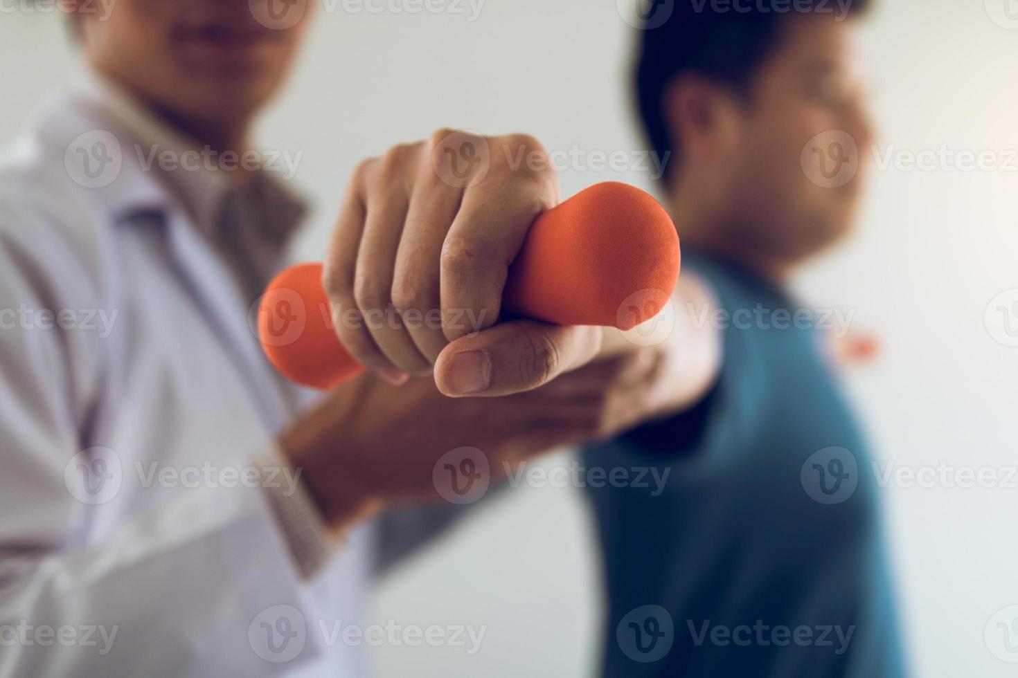 Fisioterapeuta masculino joven asiático que ayuda al paciente con ejercicios de levantamiento de pesas en el consultorio. foto