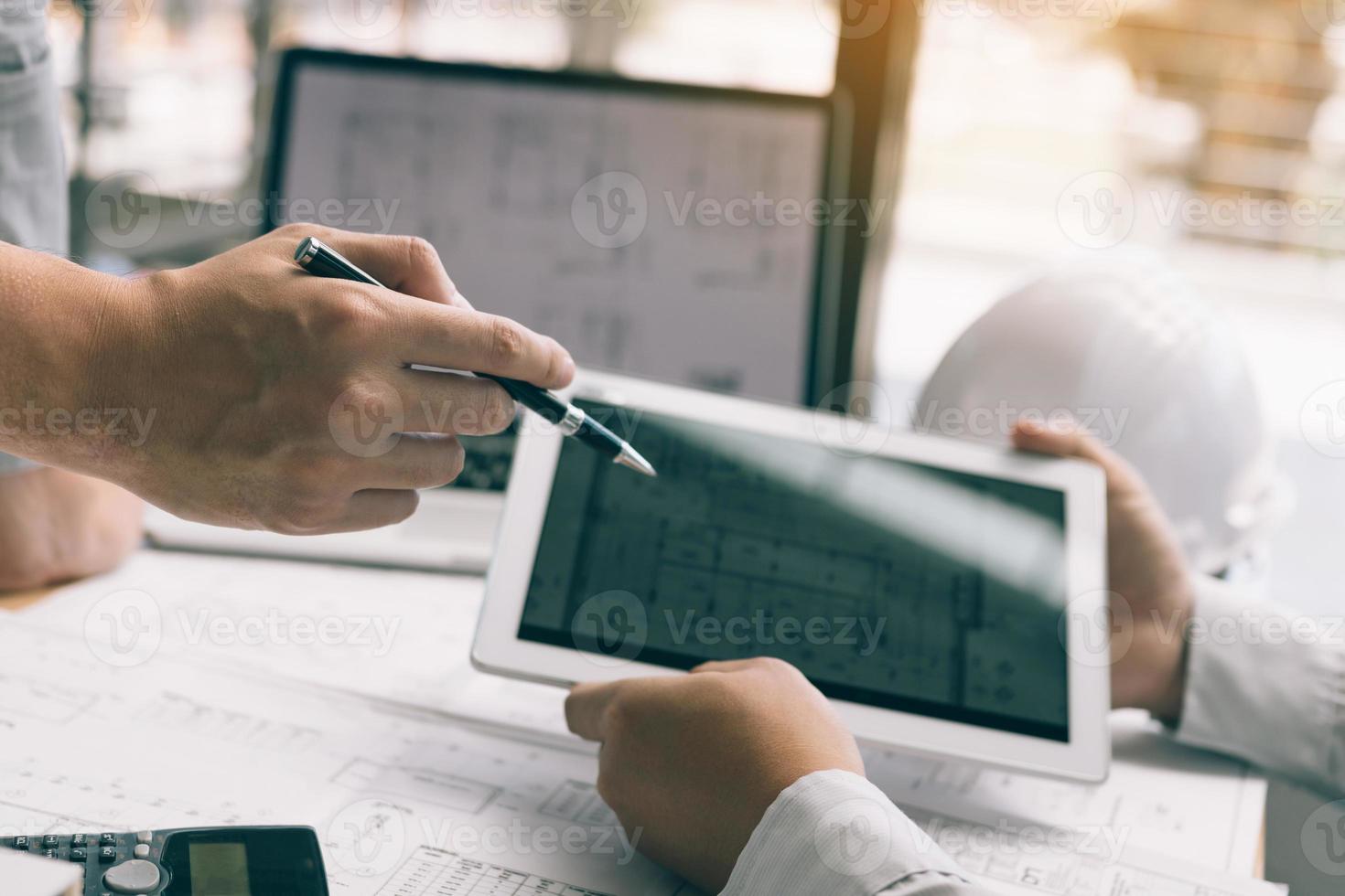 Two engineering working together and using digital tablet looking blueprint and analysis with architectural plan on desk. photo