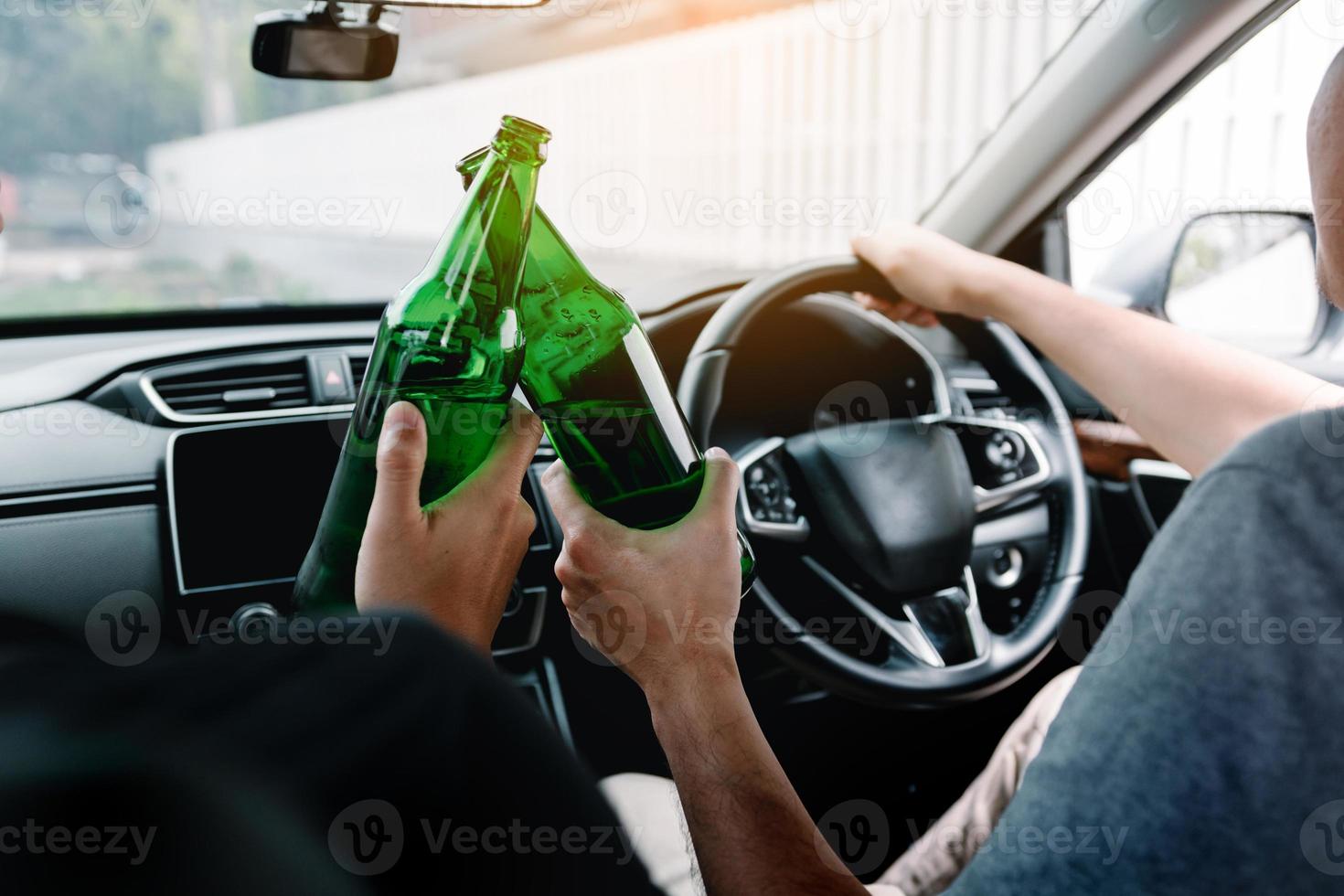 Two male friends are celebrating in the car while they are clinking beer bottle together. photo