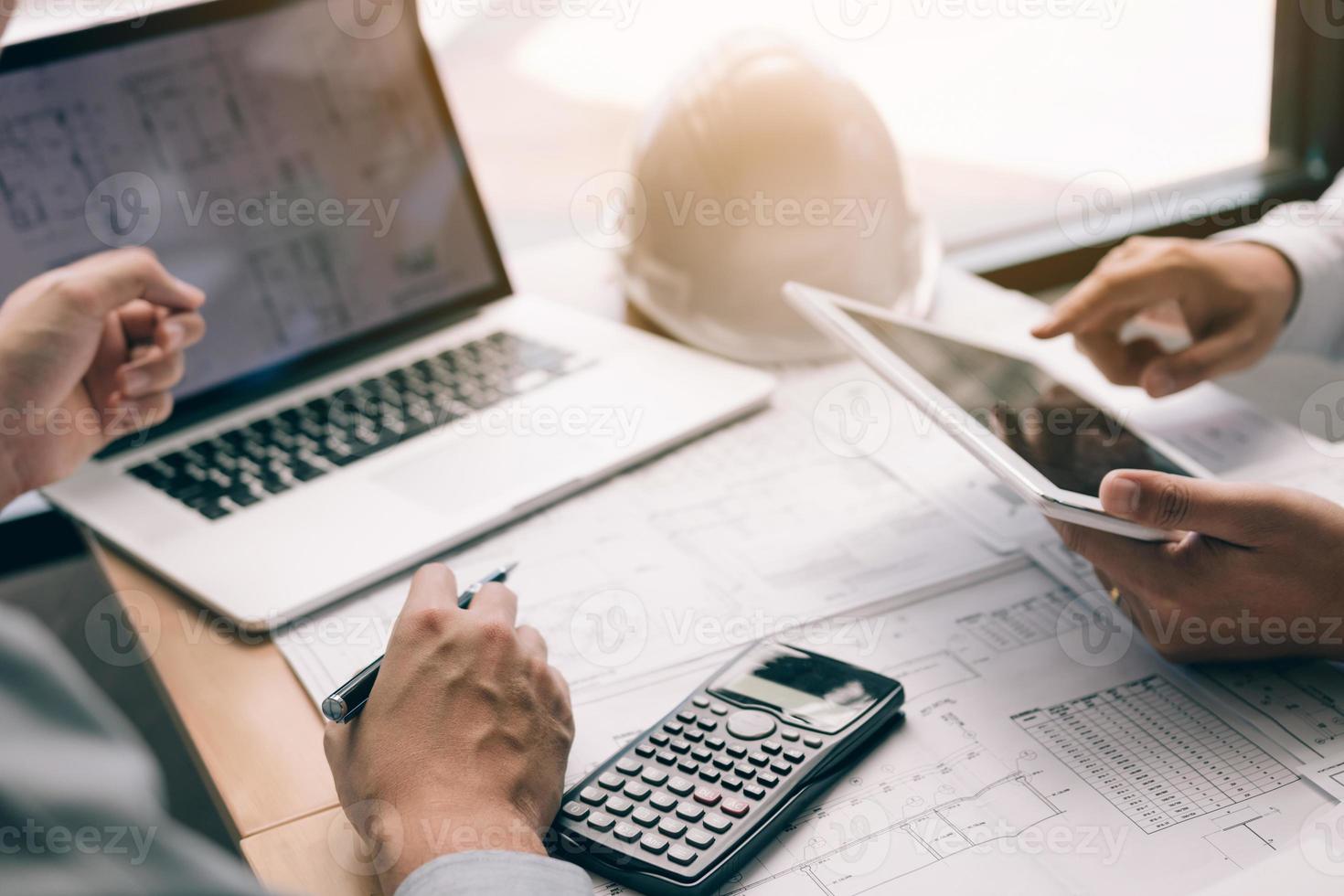 Two engineering working together and using digital tablet looking blueprint and analysis with architectural plan on desk. photo