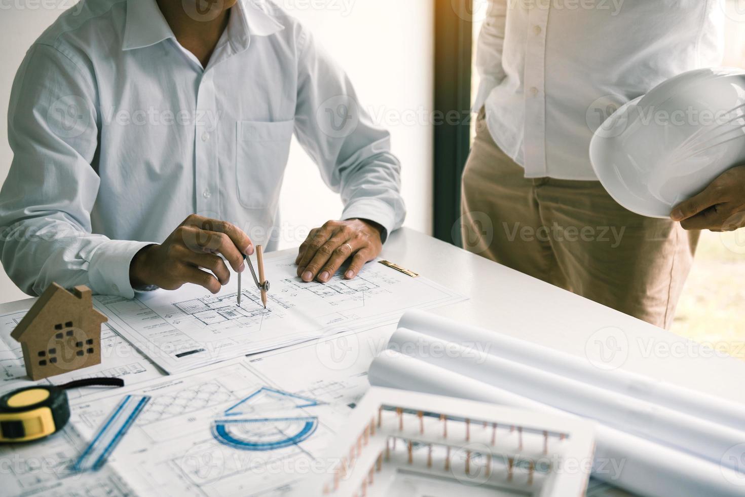 Two engineering working together and using compass looking blueprint and analysis with architectural plan on desk. photo