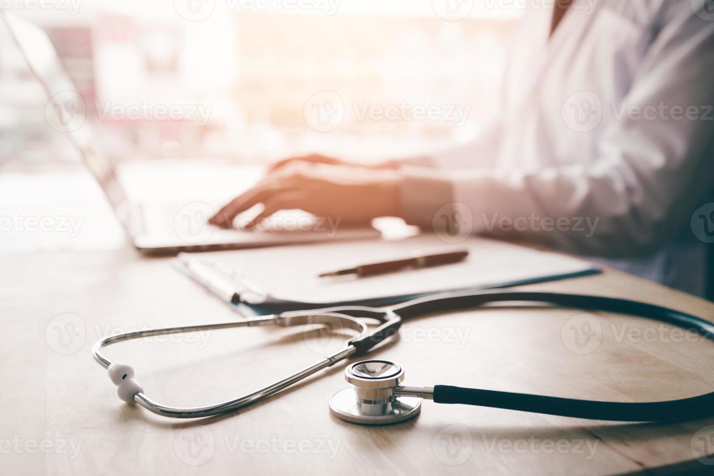 Stethoscope and background doctor using laptop at desk in clinic working on computer at room office. photo