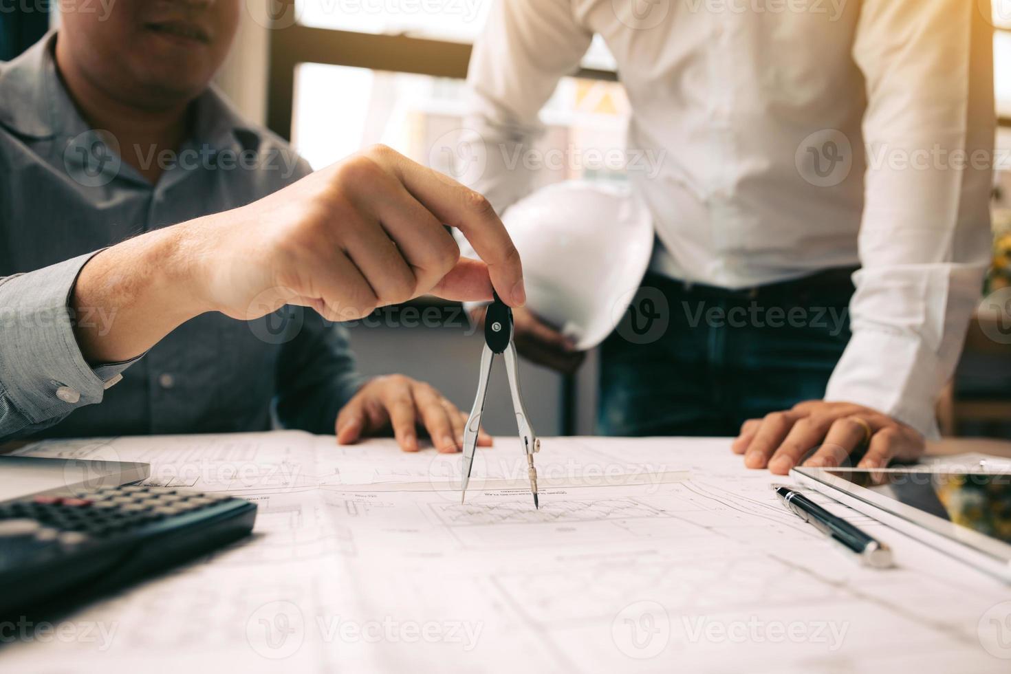 Two engineering working together and using digital tablet looking blueprint and analysis with architectural plan on desk. photo
