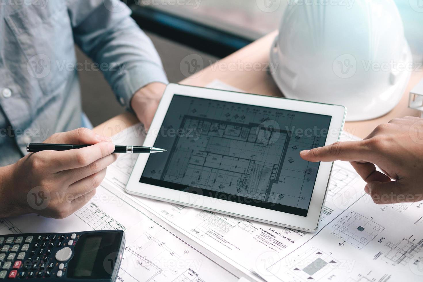 Two engineering working together and using digital tablet looking blueprint and analysis with architectural plan on desk. photo