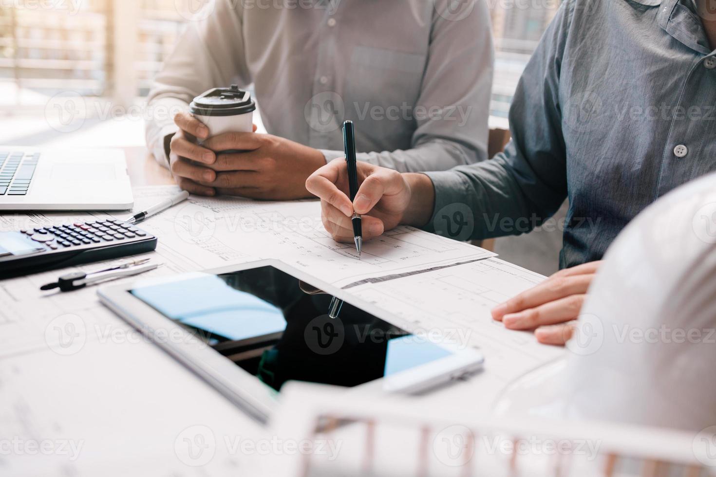 Two engineering working together and using digital tablet looking blueprint and analysis with architectural plan on desk. photo