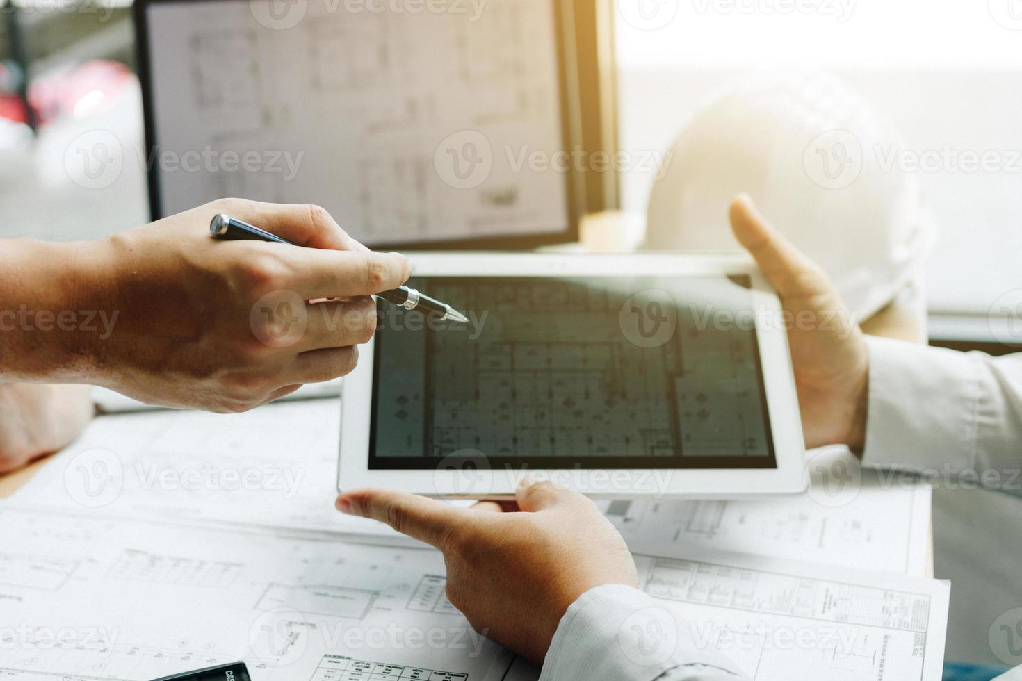 Two engineering working together and using digital tablet looking blueprint and analysis with architectural plan on desk. photo
