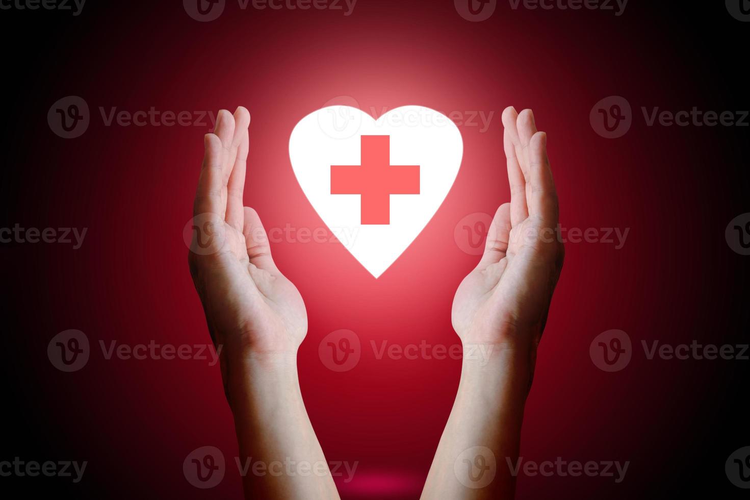 concepto de salud, mano de mujer sosteniendo y protegiendo el corazón con símbolo médico dentro sobre fondo rojo. foto