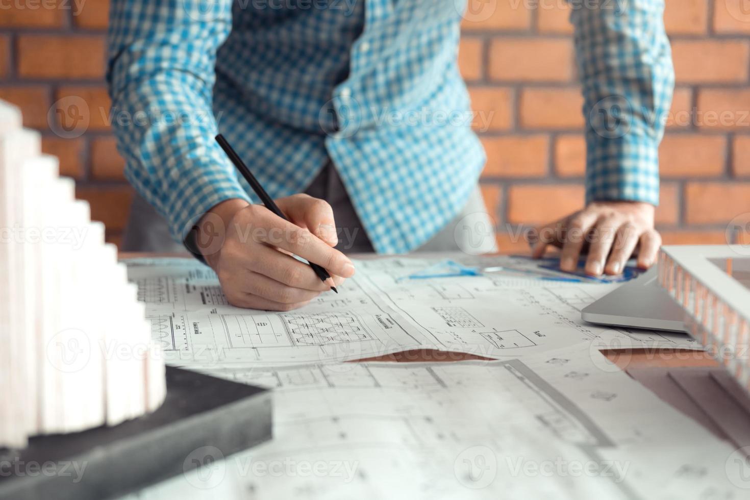 Hand of young engineering man drawing on blueprint with model on desk. photo