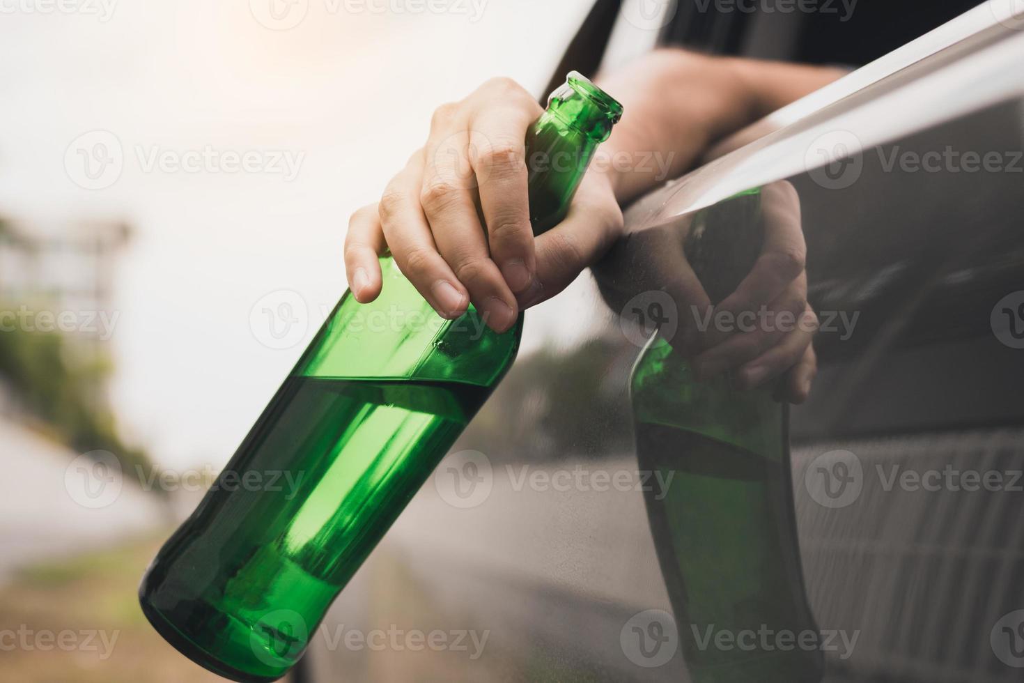 Asian man holding a bottle of beer outside the car while driving. photo