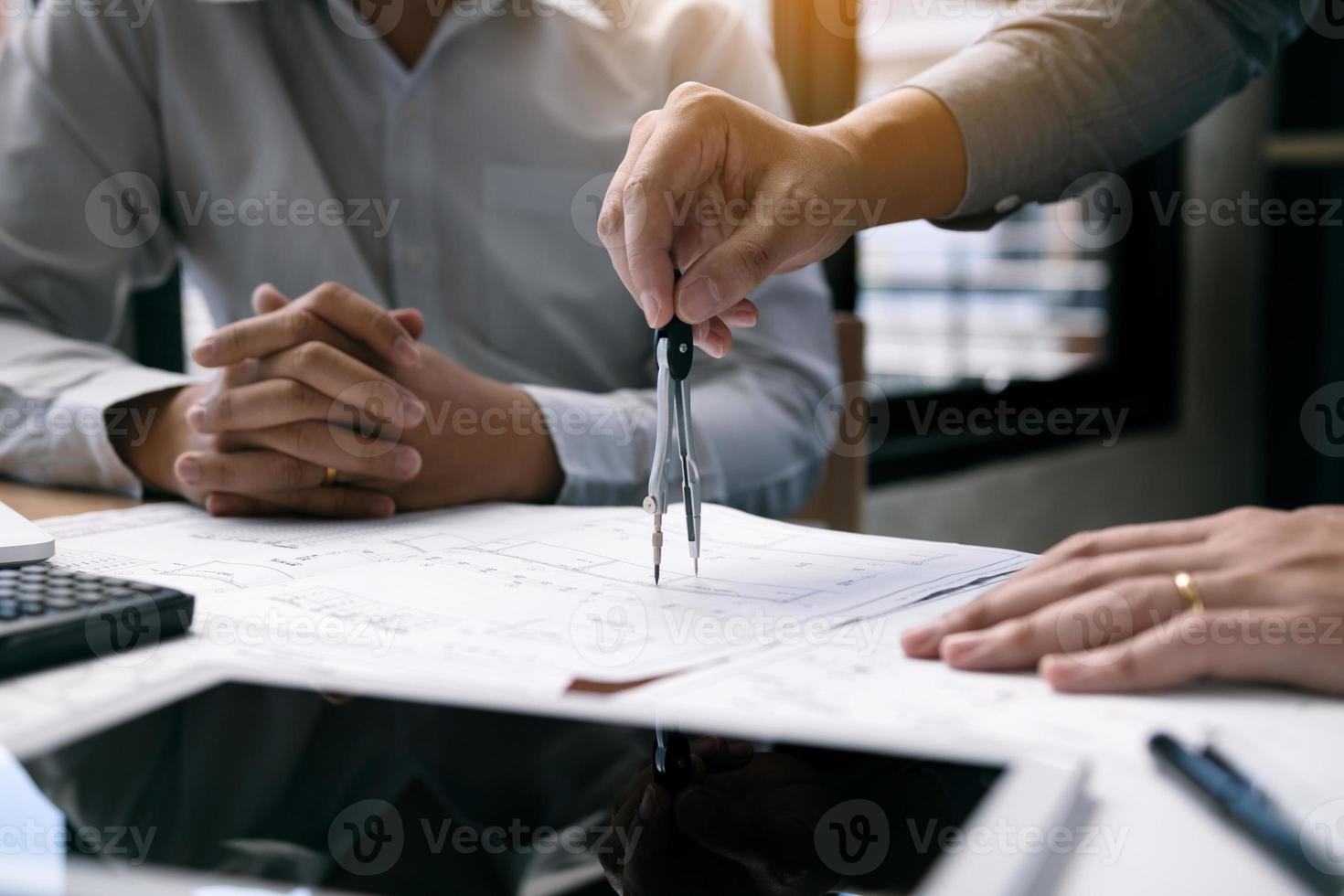 Two engineering working together and using digital tablet looking blueprint and analysis with architectural plan on desk. photo