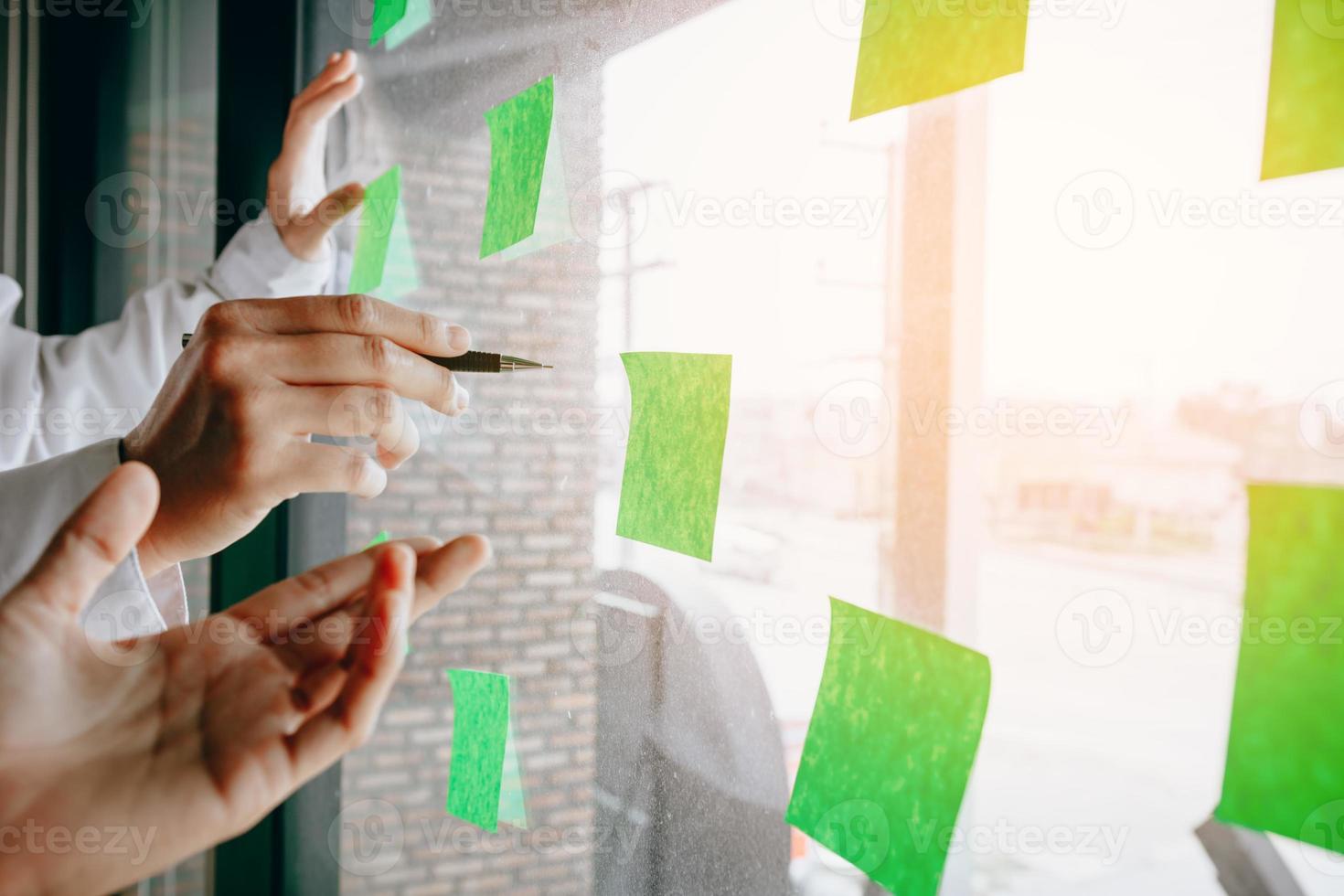 Business team with glass board room pointing ideas on adhesive notes working together. photo