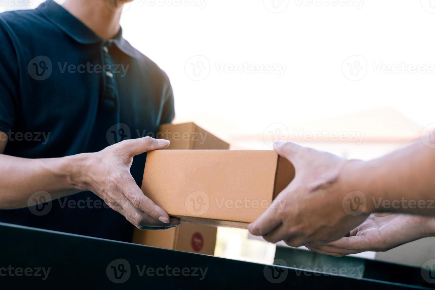 el transportista de carga asiático sostiene una caja de cartón con el paquete dentro y el destinatario está firmando el paquete. foto