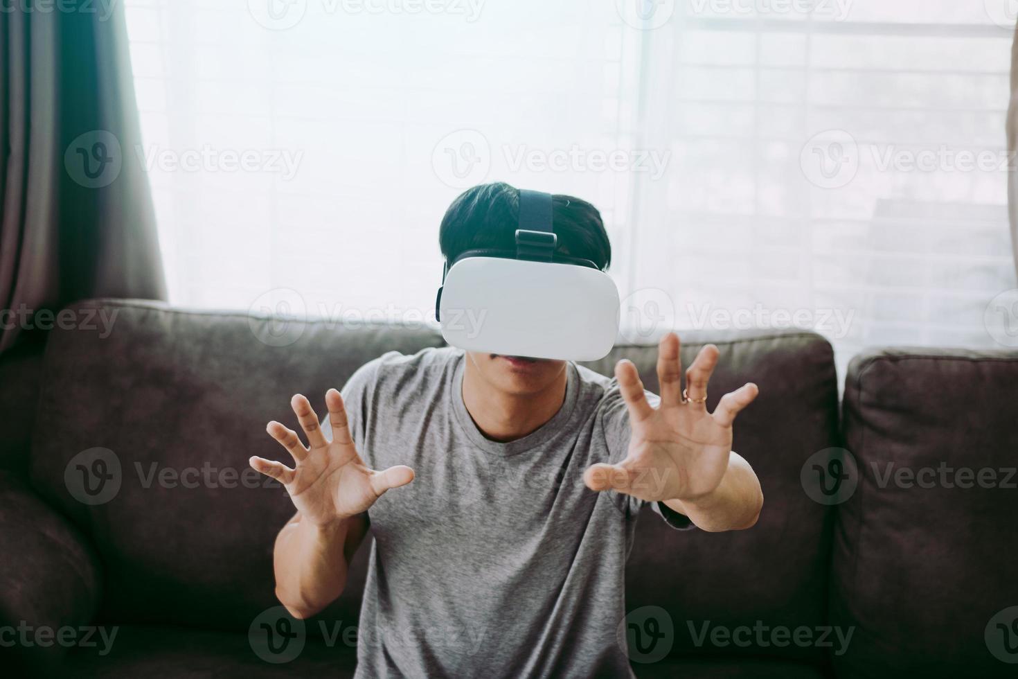 Young asian man wearing virtual reality glasses at living room for admiring virtual reality. photo