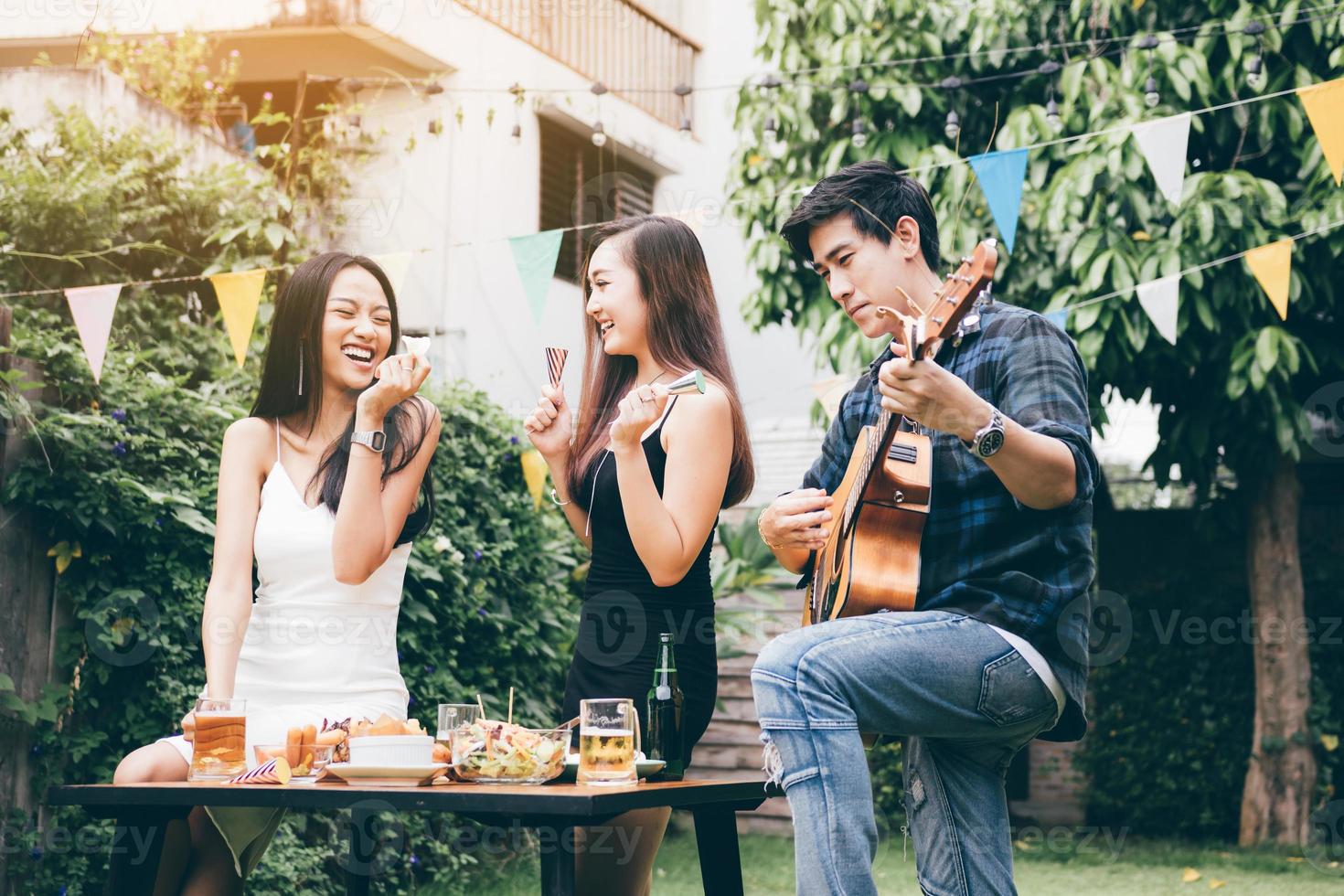 Women enjoying drinks party with guy playing guitar singing at home garden outdoors. photo