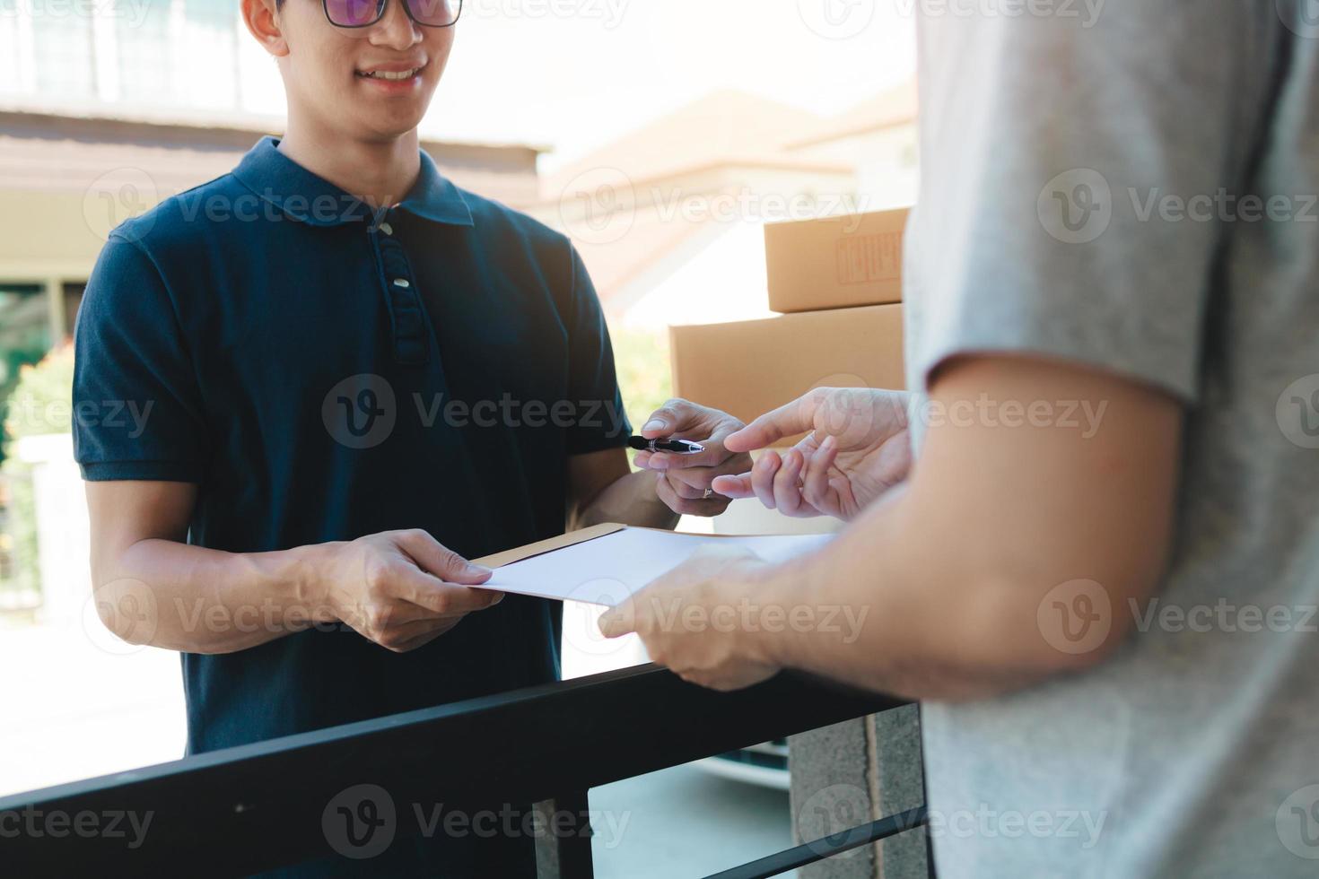 joven asiático sonriendo mientras entrega una caja de cartón a la mujer que tiene el documento para firmar la firma. foto