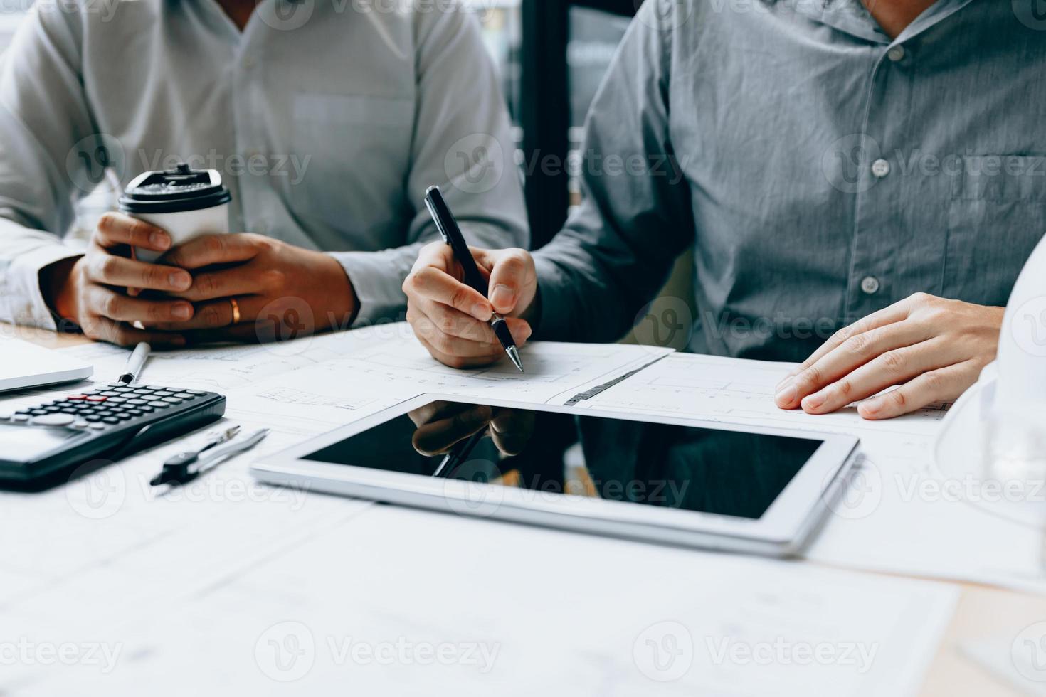 Two engineering working together and using digital tablet looking blueprint and analysis with architectural plan on desk. photo