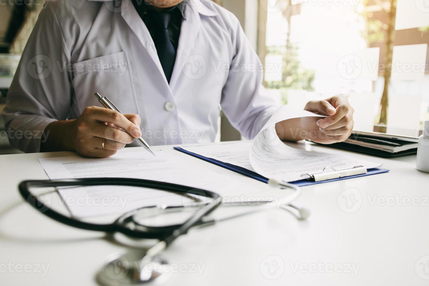 mano del médico sosteniendo la pluma escribiendo la lista de antecedentes del paciente en el bloc de notas y hablando con el paciente sobre la medicación y el tratamiento. foto