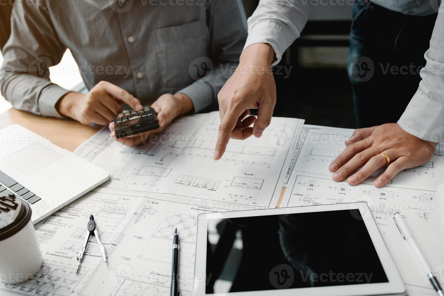 Two engineering working together and using digital tablet looking blueprint and analysis with architectural plan on desk. photo