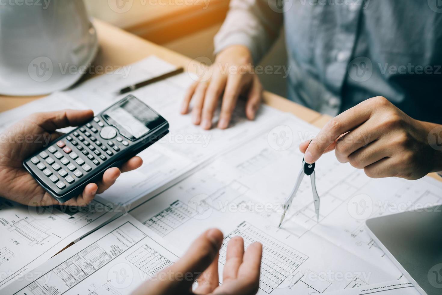 Two architect working at construction site and compass drawing pointing on blueprint with calculator calculate. photo