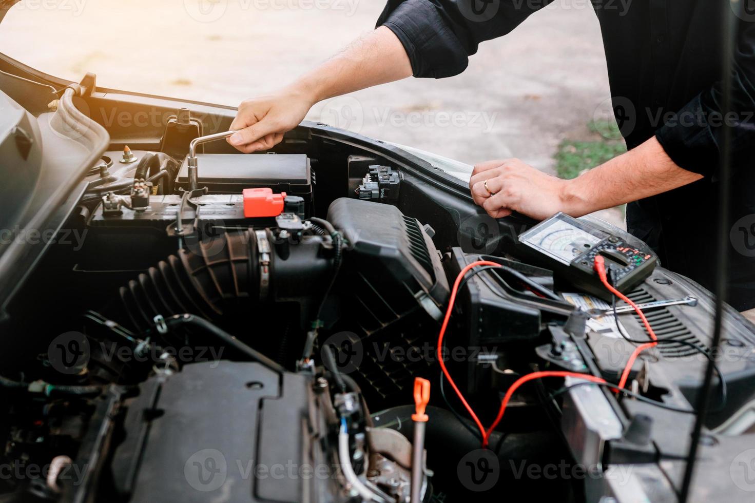 el mecánico de automóviles está revisando el motor y sosteniendo el indicador de batería. foto