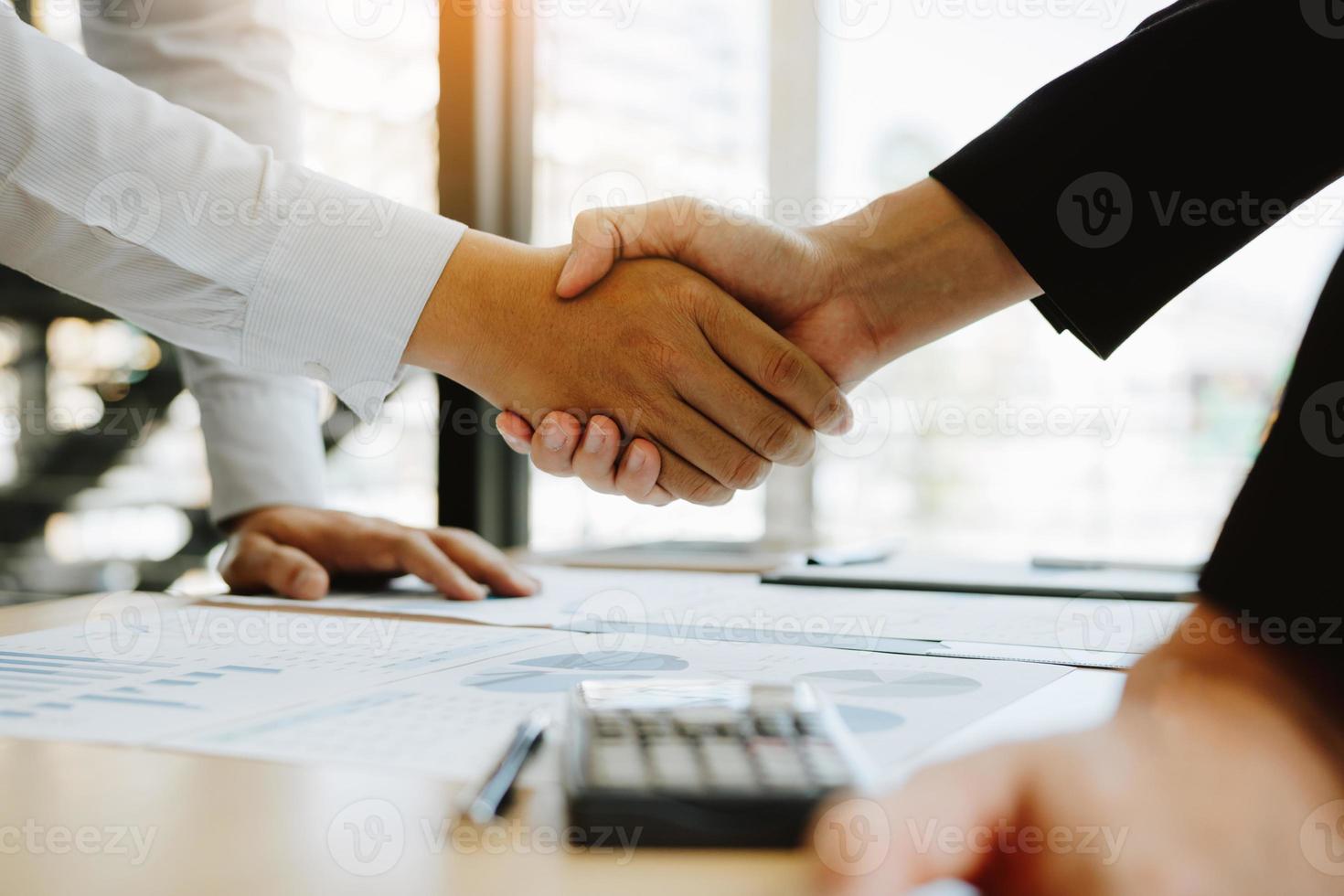 Entrepreneurs collaboration deal shaking hands in a modern office and financial paper graph on desk. photo