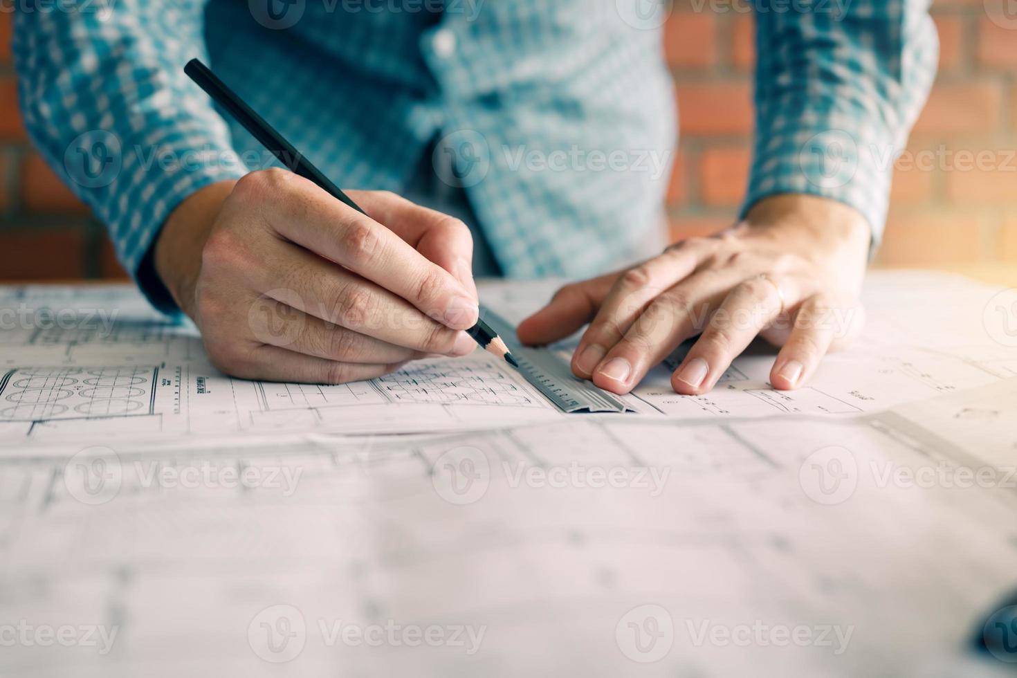 Engineering or architect reviewing blueprints and holding pencil on desk at home office. photo