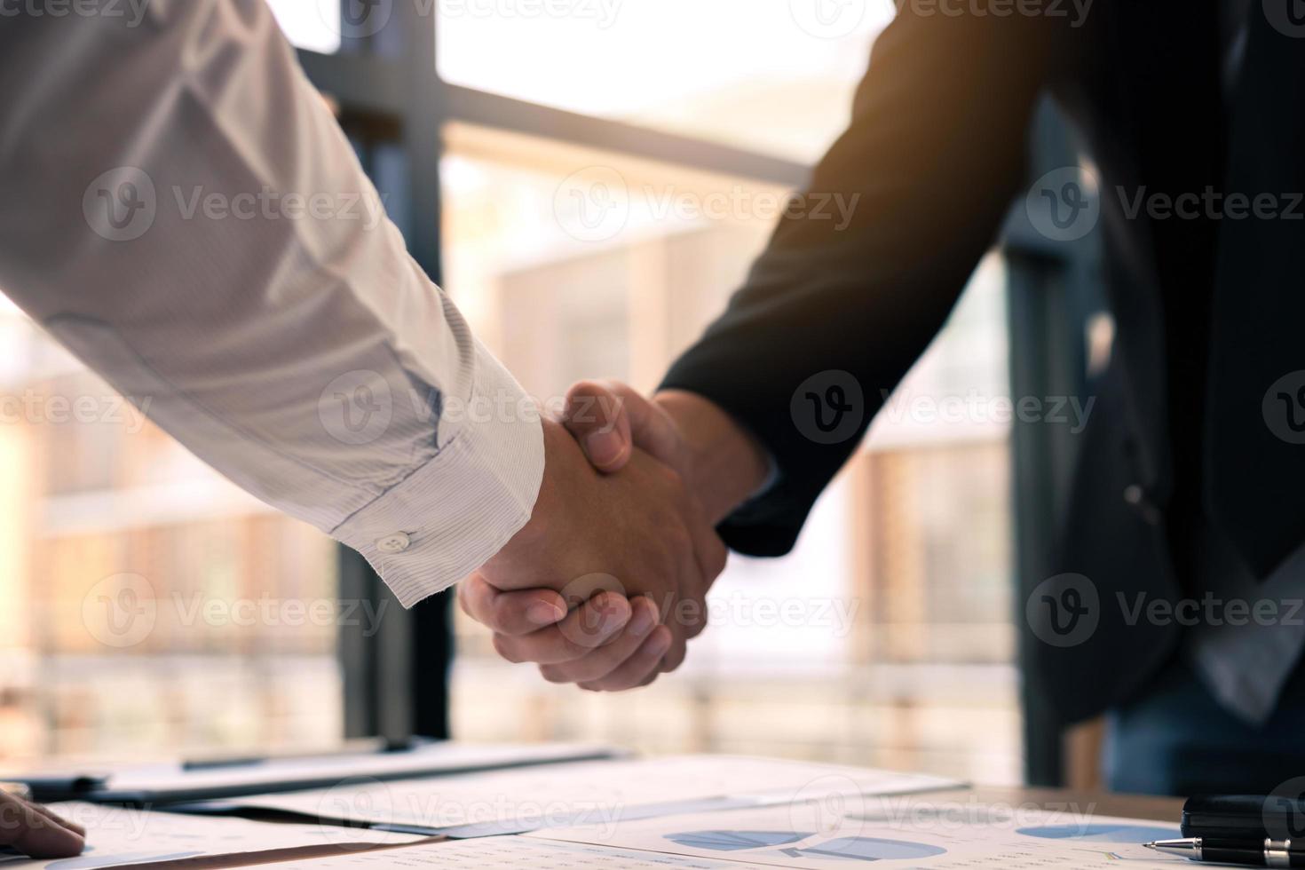 Entrepreneurs collaboration deal shaking hands in a modern office and financial paper graph on desk. photo
