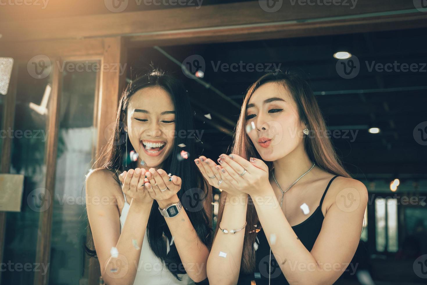 Two asian women blowing paper confetti for a celebration in his home. photo