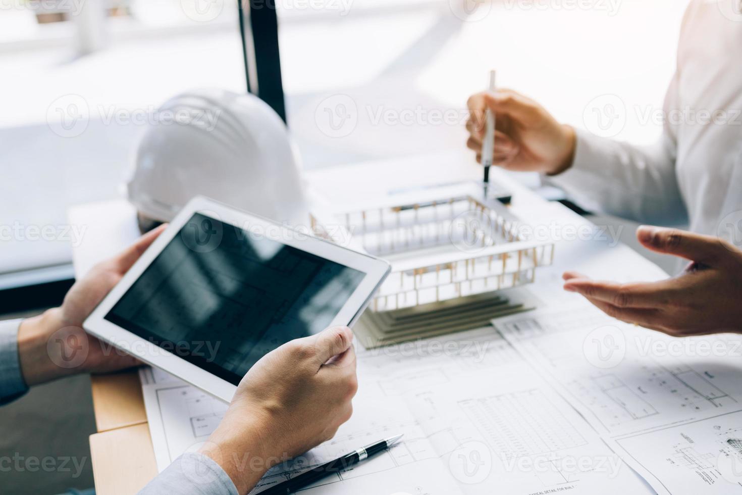Two engineering working together and using digital tablet looking blueprint and analysis with architectural plan on desk. photo