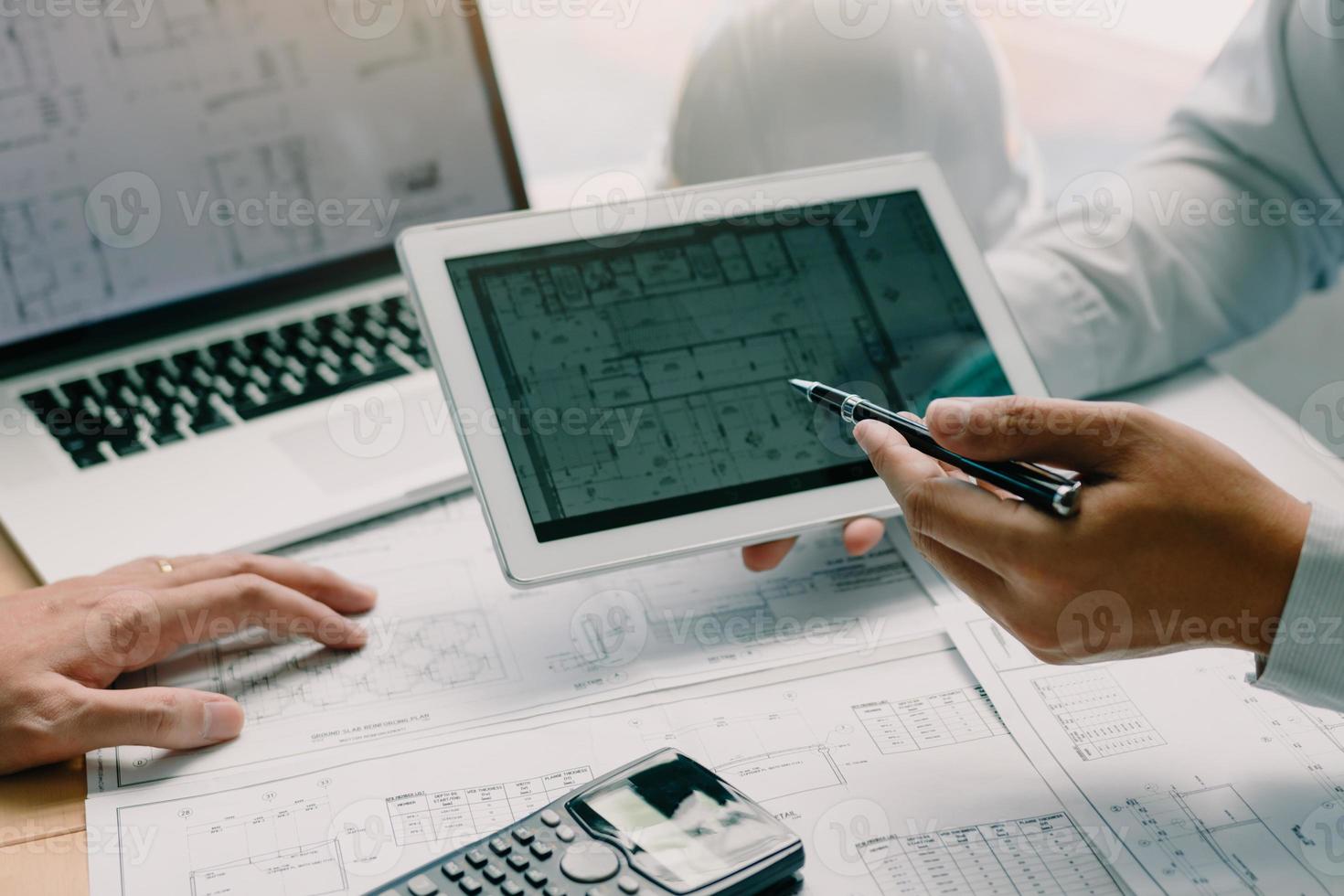 dos ingenieros trabajando juntos y usando una tableta digital buscando planos y análisis con un plan arquitectónico en el escritorio. foto