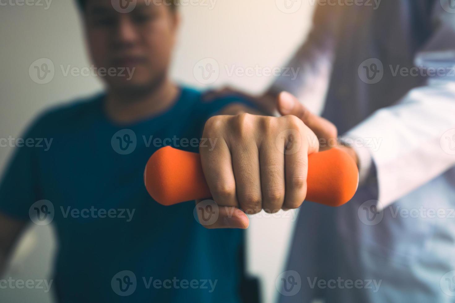 Asian physiotherapist helping a patient lifting dumbbells work through his recovery with weights in clinic room. photo