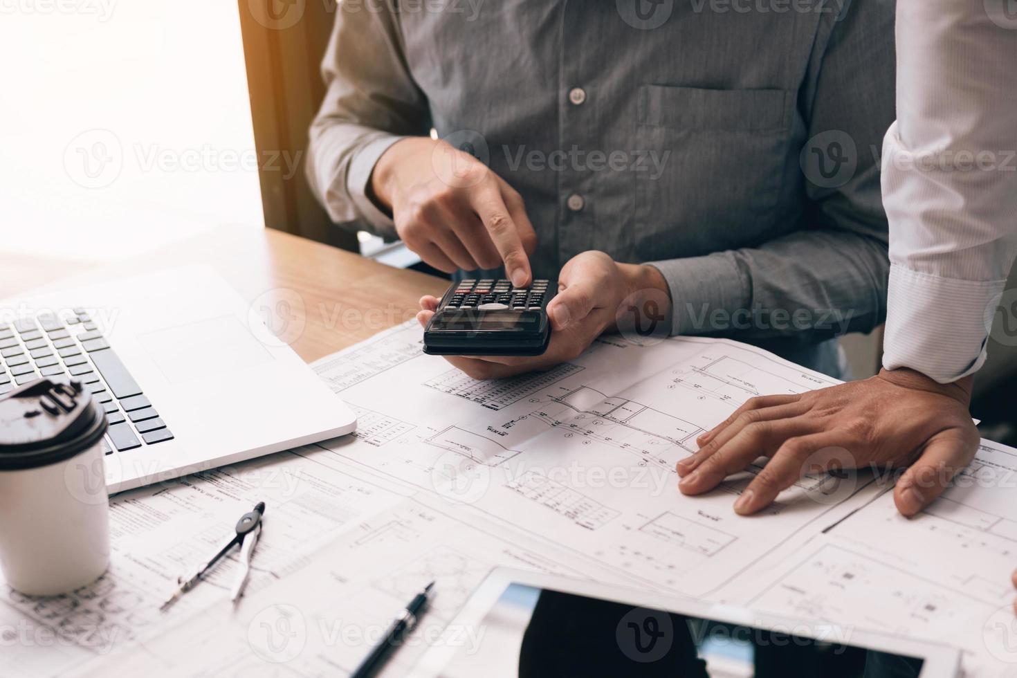 Two engineering working together and using digital tablet looking blueprint and analysis with architectural plan on desk. photo