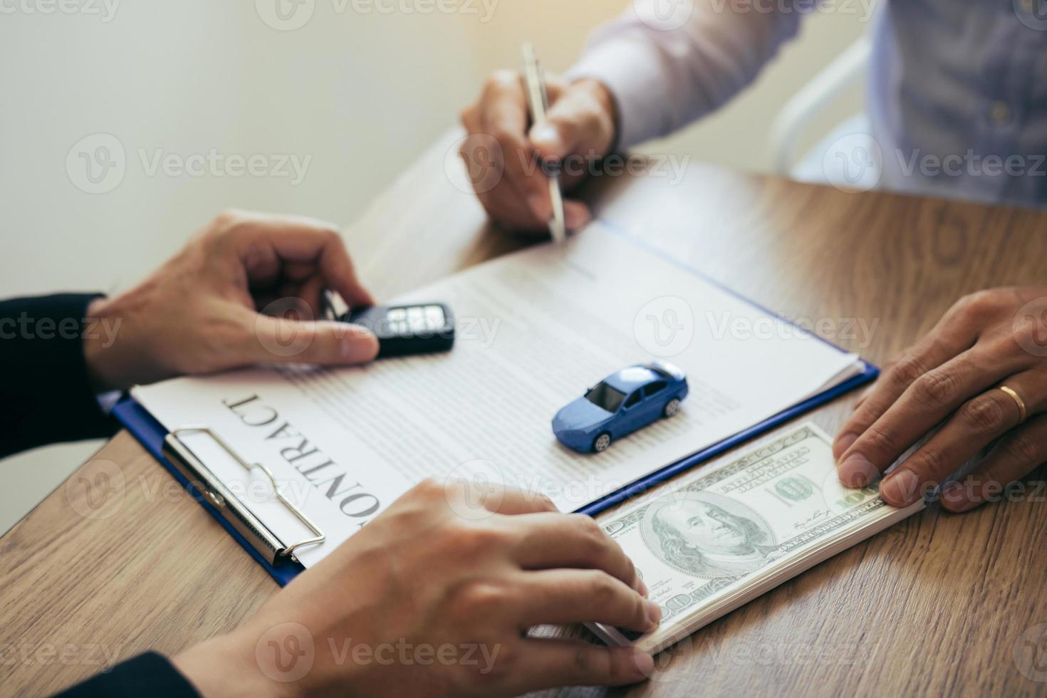 los compradores de automóviles nuevos están firmando un contrato con un vendedor de automóviles en la sala de exposición el día en que reciben el automóvil y entregan el efectivo al empleado. foto