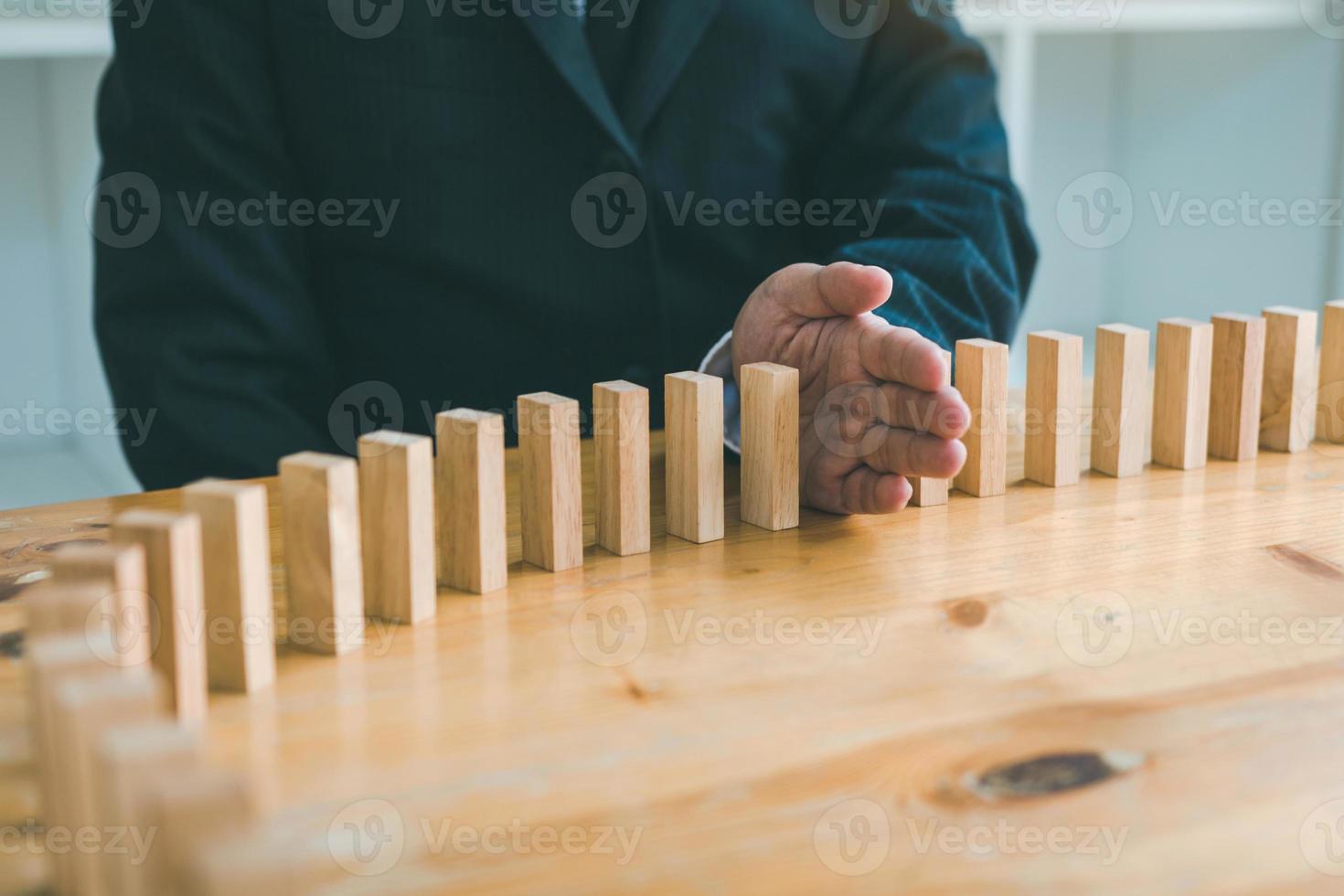 Close up hand businessman stopping wooden block from falling in the line of domino with risk concept. photo