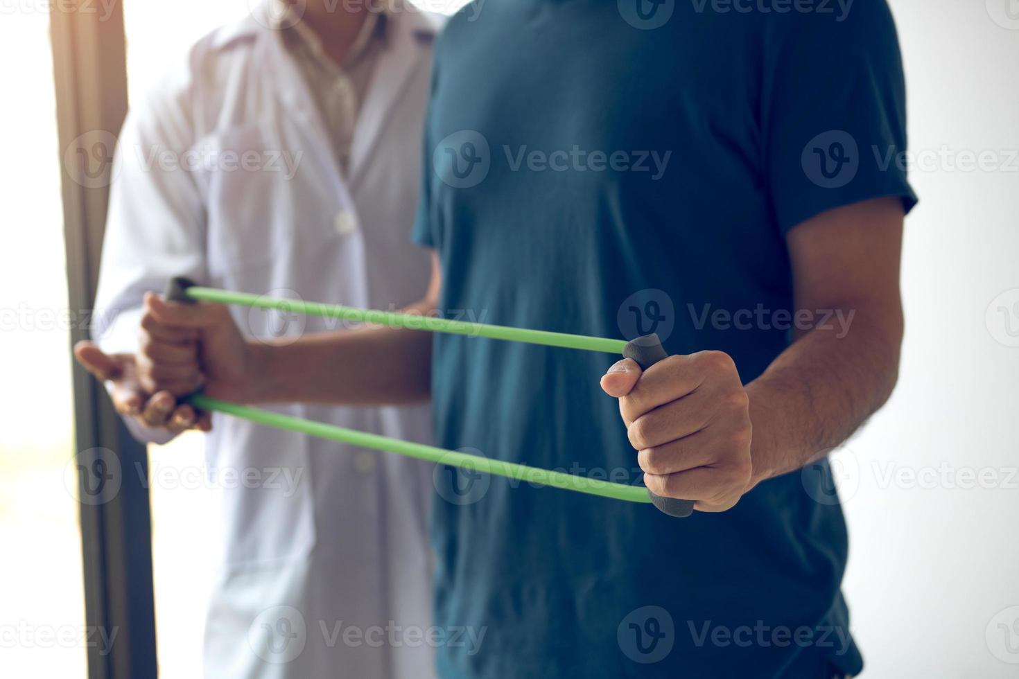 Patient doing stretching exercise with a flexible exercise band and a physical therapist hand to help in clinic room. photo