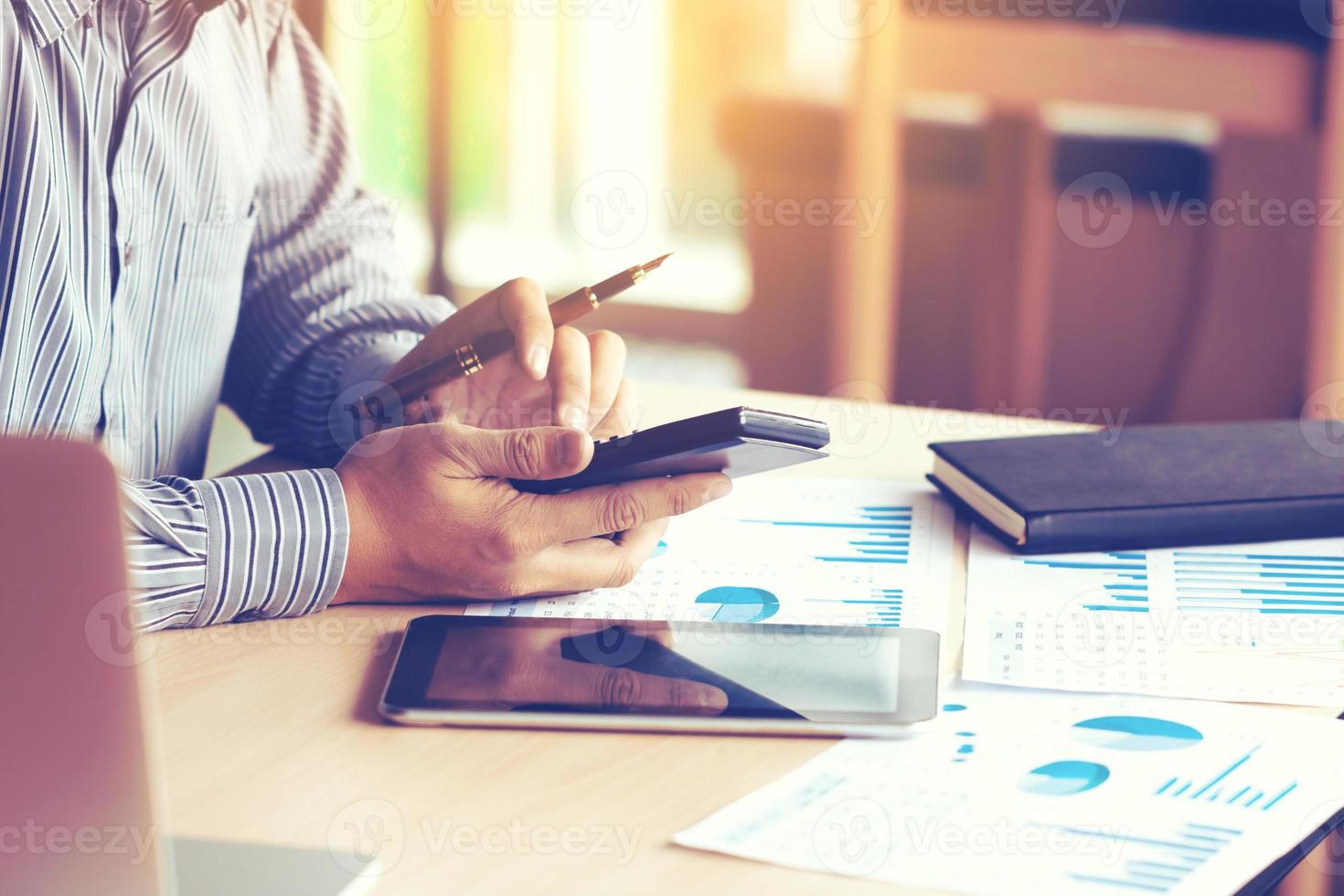 Businessman hand typing button on calculator with calculating about expenditure for company in office and apply technology with laptop and tablet for searching data result. photo