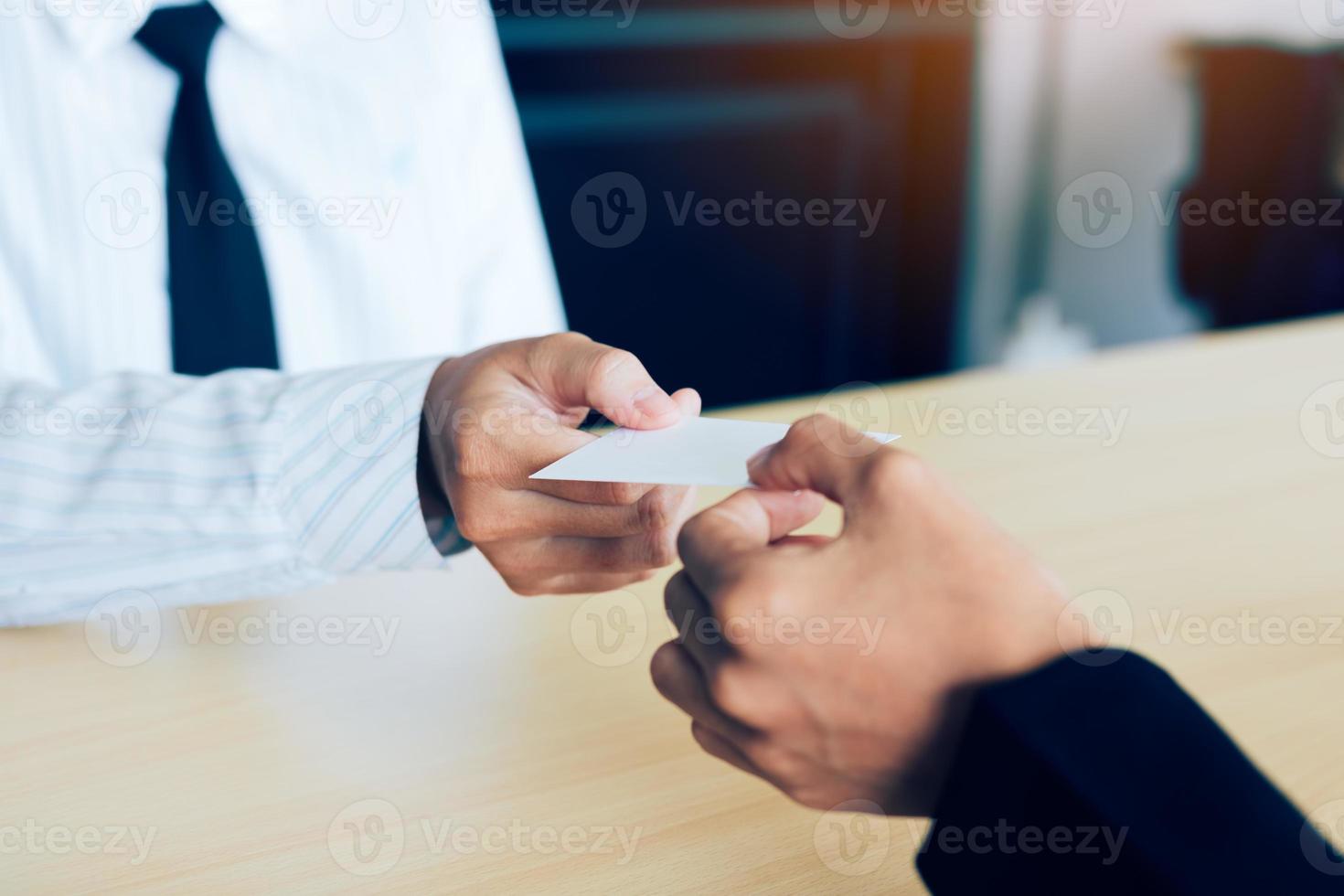 Two businessmen exchanged white business cards on a wooden table in office. photo