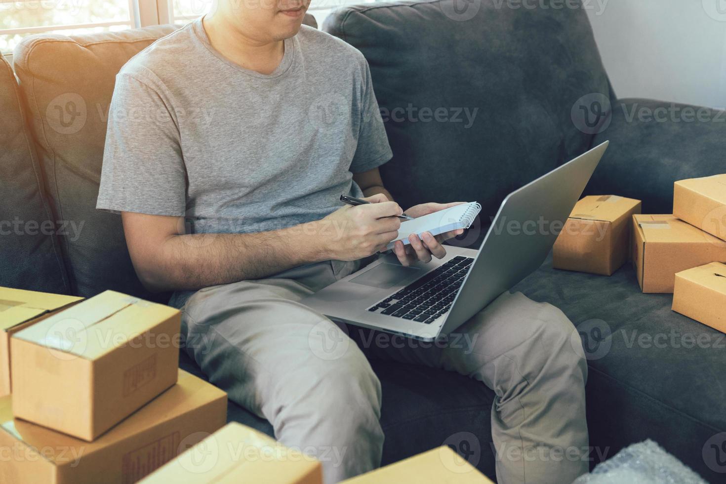 joven asiático mirando en la computadora portátil y escribiendo la lista de pedidos en papel, concepto sme. foto