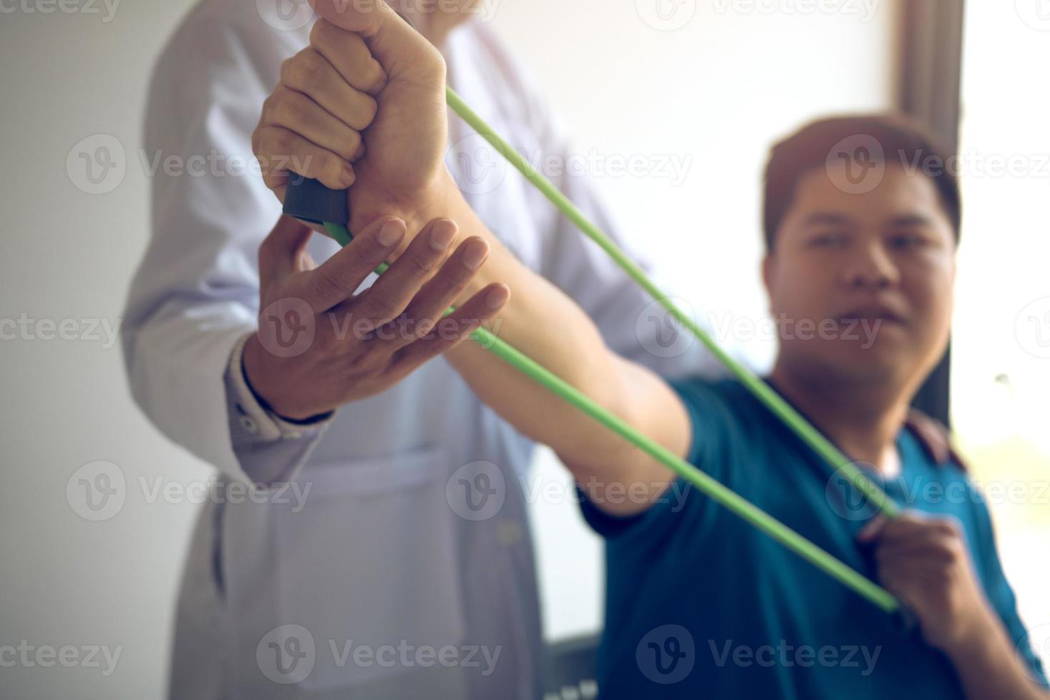 cierre el paciente de la mano haciendo ejercicio de estiramiento con una banda de ejercicio flexible y una mano de fisioterapeuta para ayudar en la sala de la clínica. foto