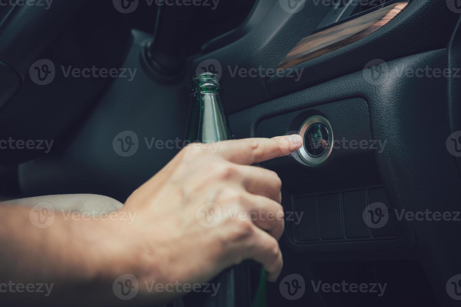 The man hand is holding a beer bottle and pressing the engine start button. photo