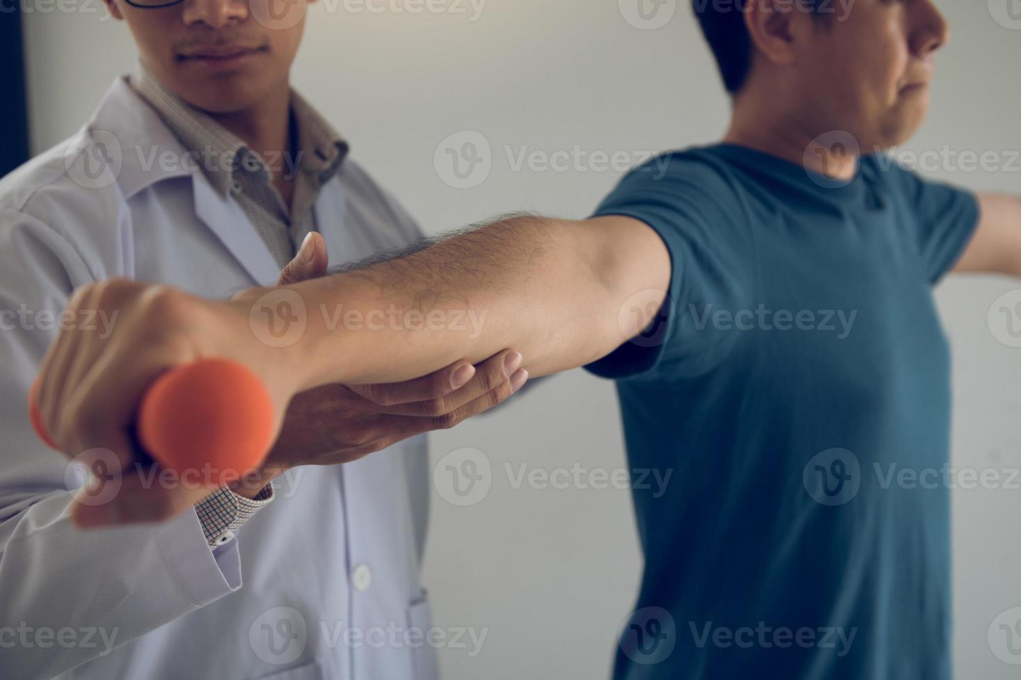 Asian physiotherapist helping a patient lifting dumbbells work through his recovery with weights in clinic room. photo