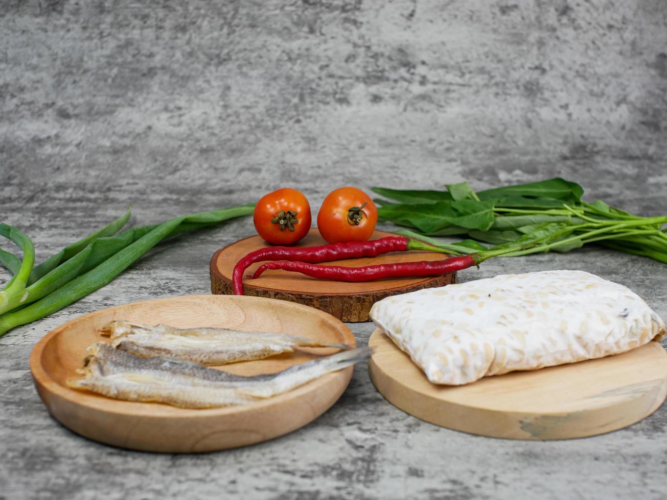 salted fish, raw tempeh and vegetables on a wooden cutting board photo