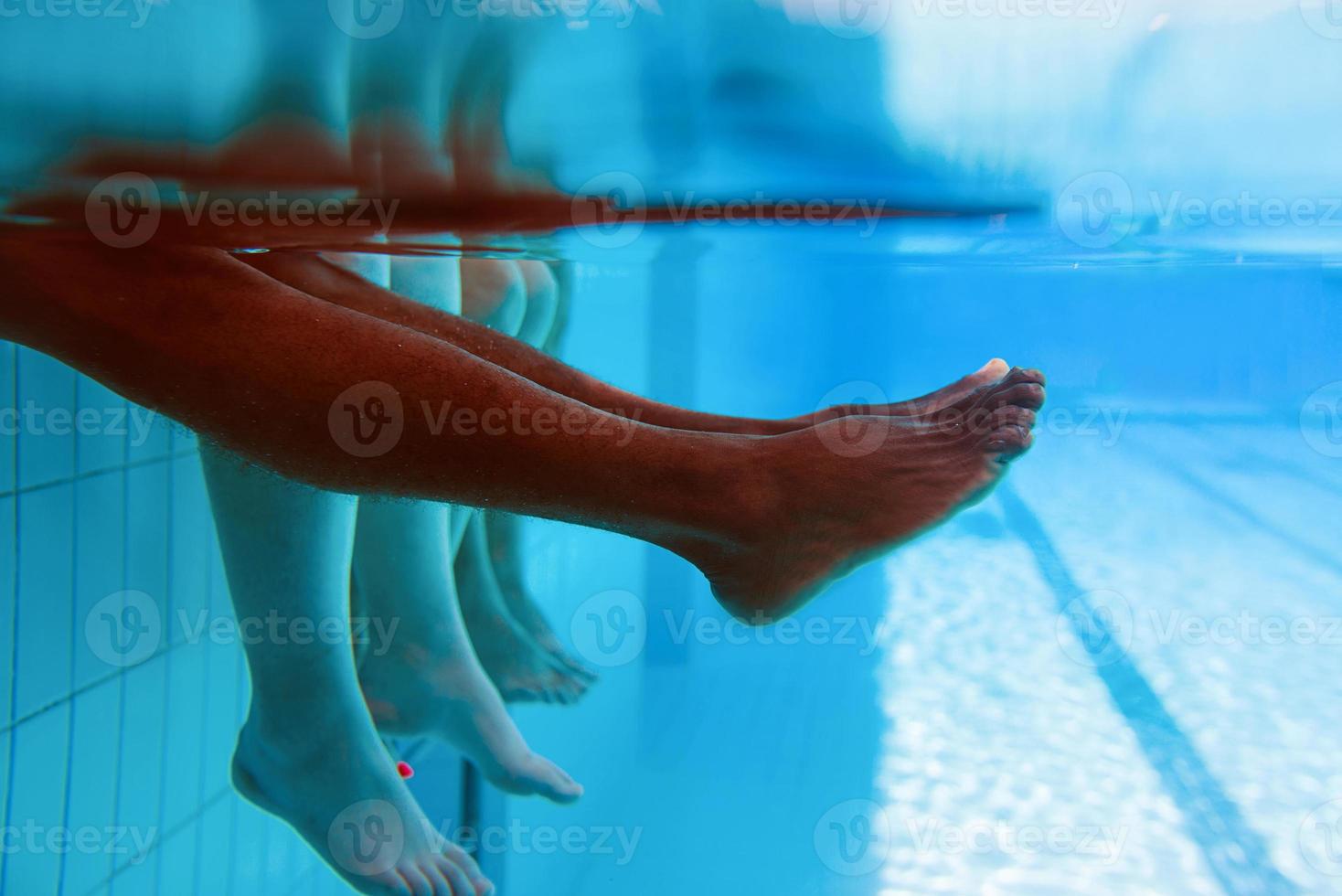 Legs of African American man with caucasian friends in swimming pool underwater. Summer. Vacation, international and sport concept. photo
