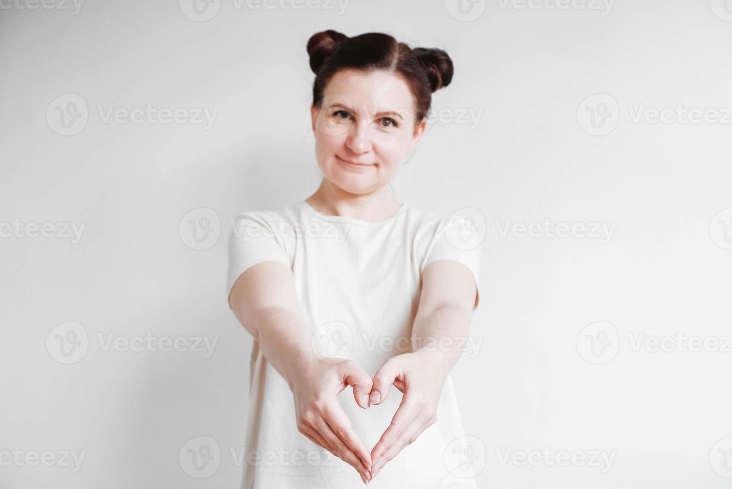 Portrait of beautifull woman making a heart shape with her fingers standing over white backgrounnd. Copy, empty space photo