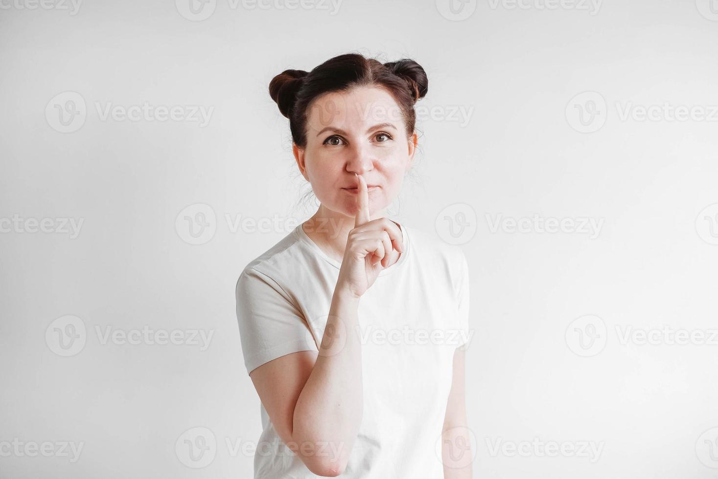 Portrait of beautifull woman with pigtails holding forefinger on her lips while standing over white backgrounnd, asking to keep secret. Copy, empty space photo