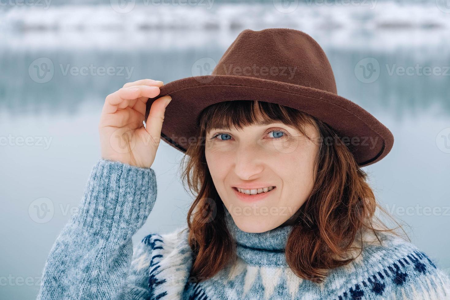 Portrait of a smiling woman in a brown hat and sweater on a background of winter landscape photo