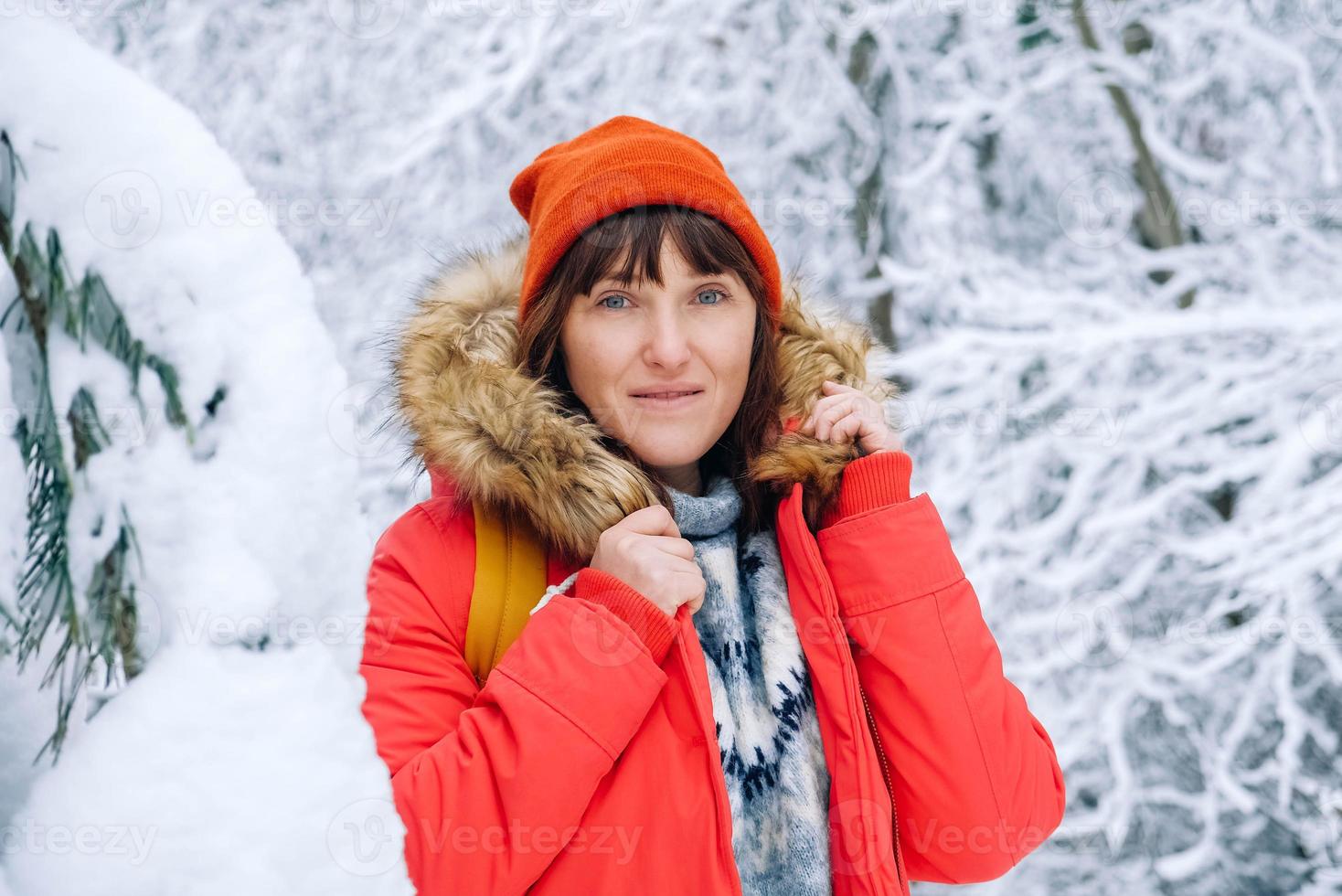 Portrait of a woman in a red warm jacket and hat in a snowy winter forest. Copy, empty space for text photo