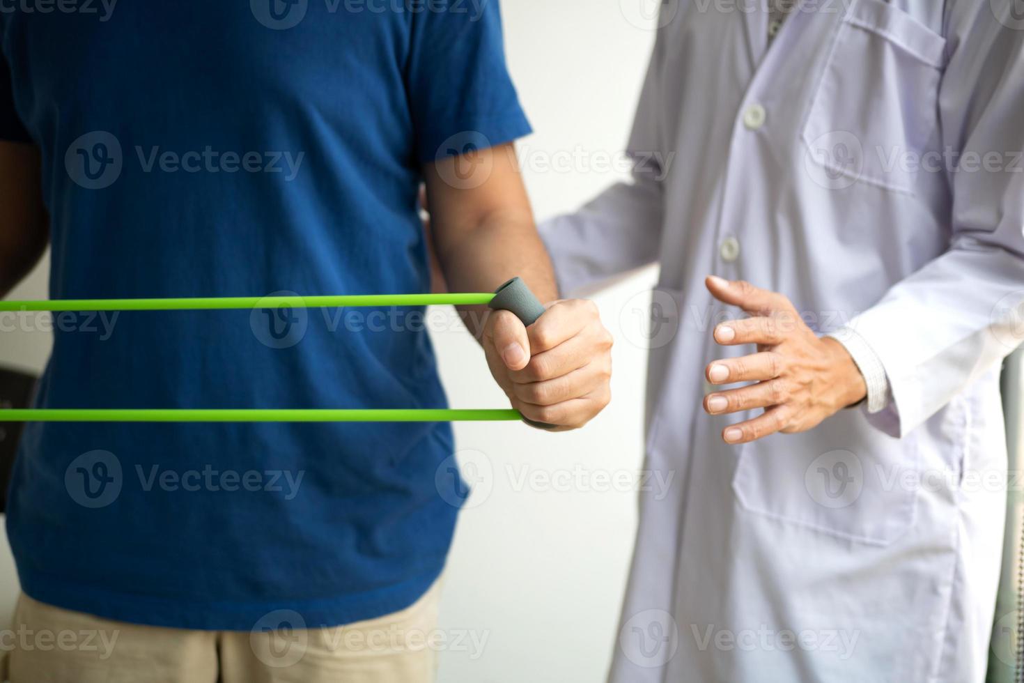 paciente haciendo ejercicio de estiramiento con una banda de ejercicio flexible y una mano de fisioterapeuta para ayudar en la sala de la clínica. foto