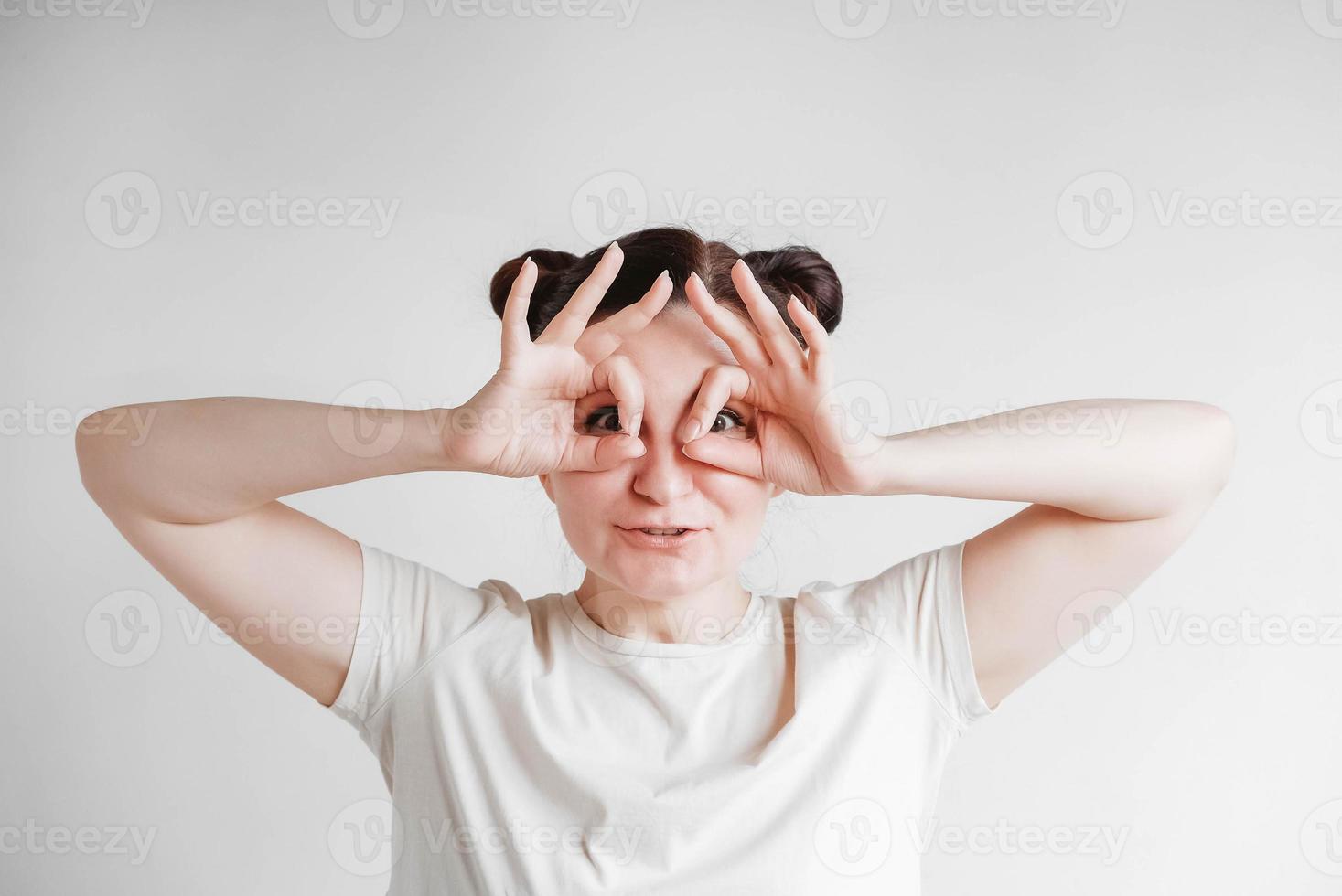 Portrait of a beautiful woman with her hands emitting glasses and a funny face wearing a T-shirt on a white background. Copy, empty space photo