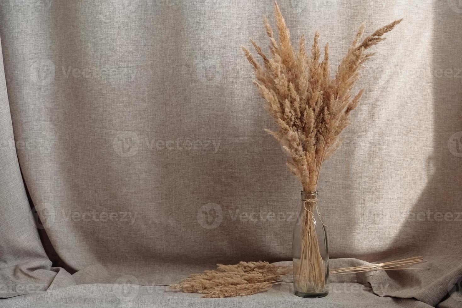 bodegón de un ramo de flores secas en una botella de vidrio sobre un fondo de tela de lino. rústico. boho lugar para texto o publicidad foto